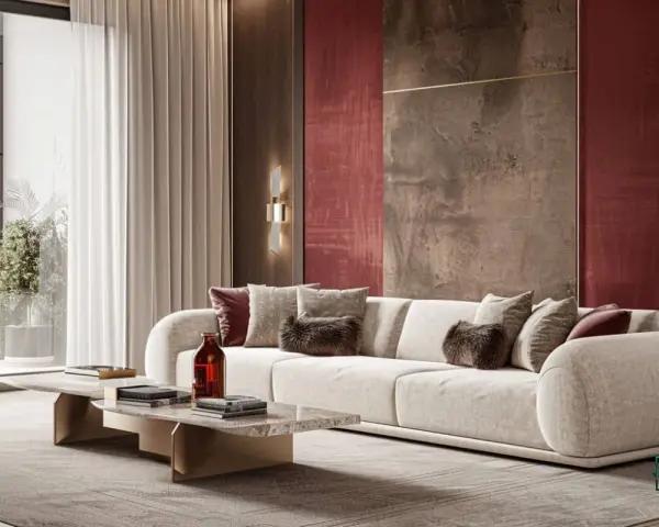 Luxuriöses Wohnzimmer mit einem cremefarbenen Sofa, das mit Kissen in verschiedenen Texturen und der Akzentfarbe bordeaux dekoriert ist. Die Wand hinter dem Sofa ist in einem tiefen Rotton gehalten.