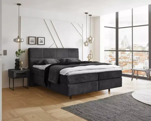 Ein modernes Schlafzimmer mit einem dunklen Boxspringbett ja oder nein? Helle Wände, Holzboden und ein Fenster mit Stadtblick.