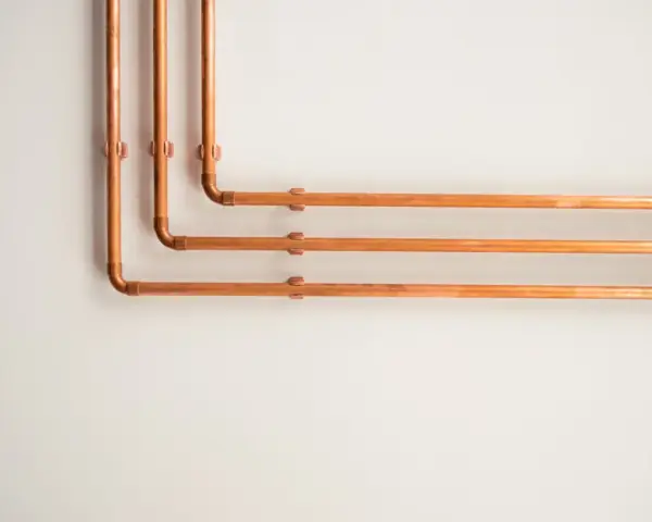 Kupferrohre an einer weißen Wand, die sich in einem rechten Winkel biegen. Tolle rohrverkleidung ideen für ein industrielles oder modernes Design.