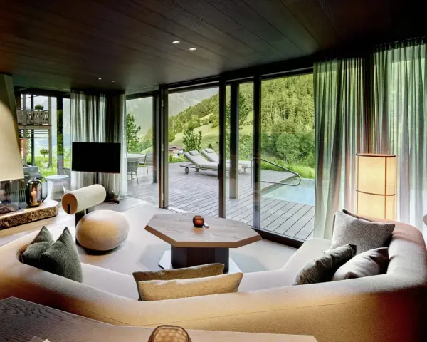 Gemütliches Wohnzimmer mit Kamin, großem Sofa und Bergblick. Die luxuriöse Chalet-Inneneinrichtung strahlt Wärme und Eleganz aus.