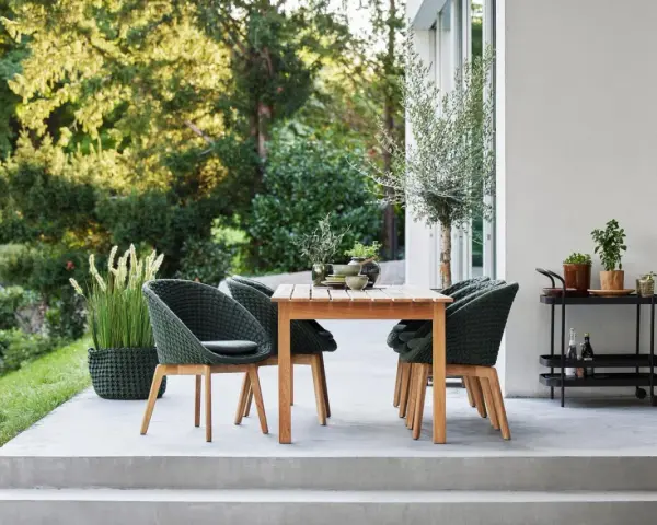 Einladende Sitzgruppe auf einer modernen Terrasse, perfekt für die nächste terrasse renovieren. Grüne Korbsessel und Holztisch laden zum Verweilen ein.