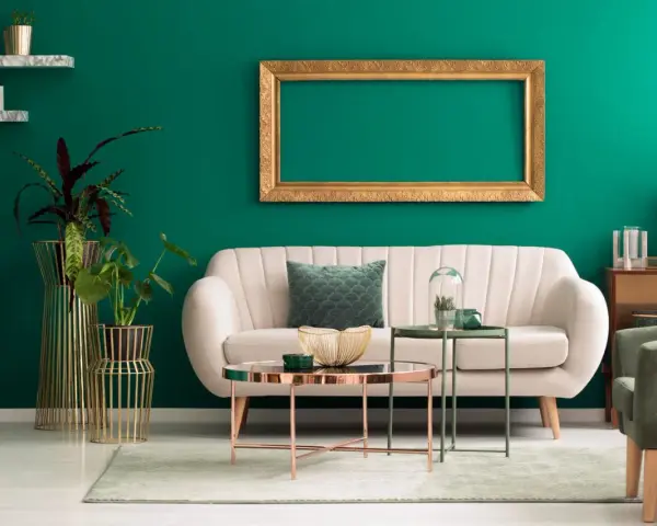 Ein helles Sofa und goldene Akzente harmonieren perfekt mit der petrolfarbenen Wand. Welche Farbe passt zu petrol? Hier sehen wir eine elegante Kombination.