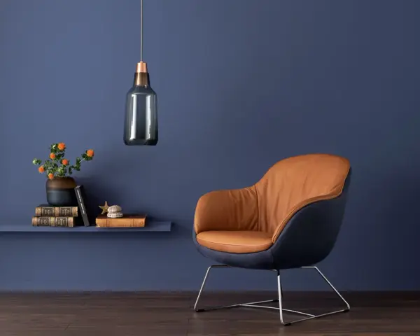 Ein Sessel mit braunem Leder und dunkelblauem Stoff vor einer blauen Wand. Orange Blumen auf einem Regal zeigen, welche Farbe passt zu Blau.