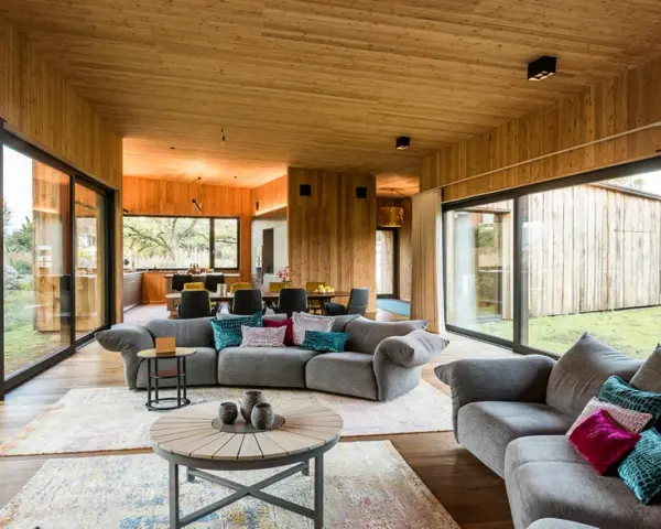 Gemütliches Wohnzimmer mit holzverkleideten Wänden und Decke, das zeigt, wie man eine holzdecke modern gestalten kann. Große Fensterfronten bieten Blick ins Grüne.