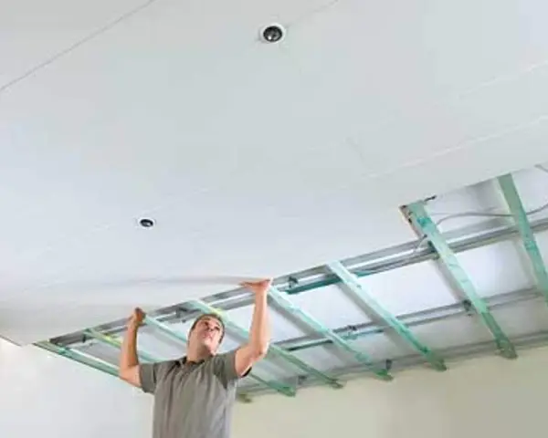 Mann verkleidet die Decke mit Gipskartonplatten. Die Unterkonstruktion ist sichtbar.