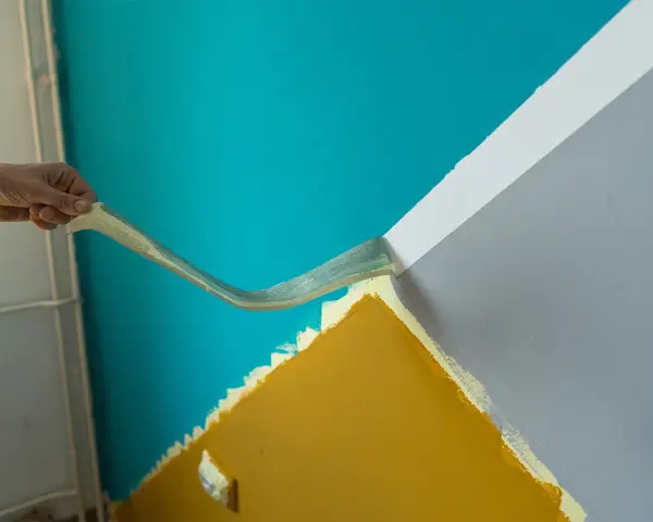 Hand zieht Klebeband ab, um eine scharfe Kante beim Wand malen zu schaffen. Türkis trifft auf Grau und Ockergelb.