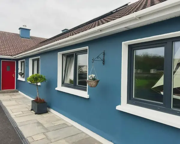 Ein blaues Haus mit roten Tür und dunklen Kunststofffenstern. Die Fensterrahmen sind in einem eleganten Anthrazit gehalten, was die modernen Kunststofffenster Farben unterstreicht.