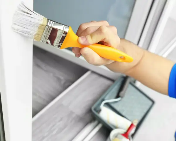 Mit welcher Farbe kann man Kunststoff streichen? Ein Pinsel mit weißer Farbe wird auf einen weißen Kunststoffrahmen aufgetragen.