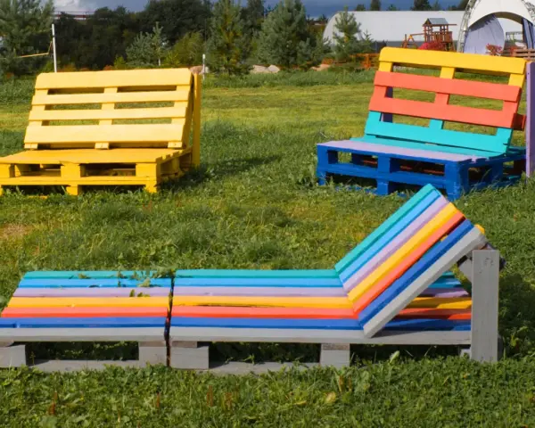 Bunte Palettenmöbel im Garten: Eine gelbe Bank, eine mehrfarbige Sitzbank und eine bunte Liege laden zum Entspannen ein. Paletten streichen ohne schleifen ist hier die Devise.