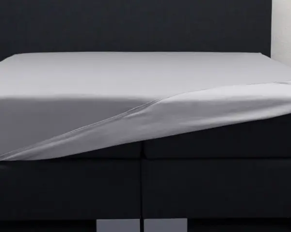 Ein graues Spannbettlaken wird über ein Boxspringbett gezogen. So beziehe ich ein Boxspringbett – einfach und schnell.