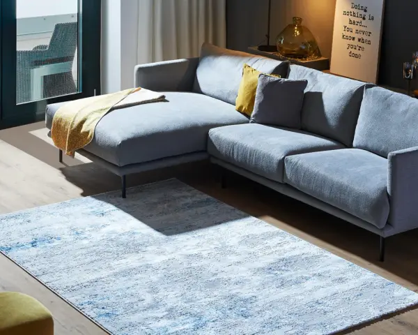 Ein moderner Wohnbereich mit einem grauen Ecksofa und einem Teppich, der richtig platziert unter dem Sofa liegt.