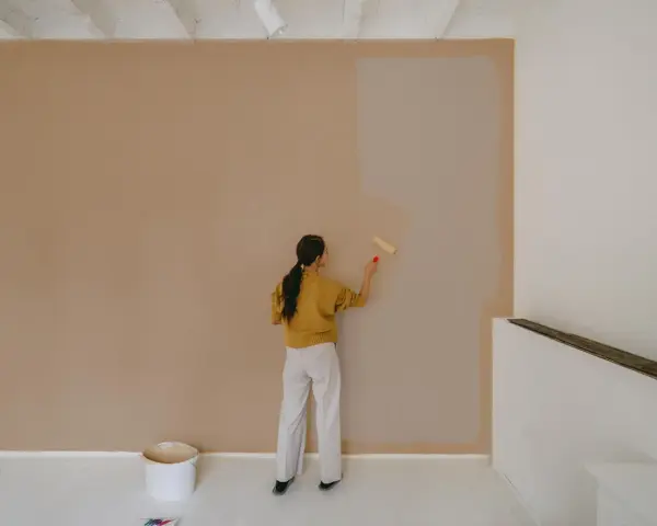 Frau streicht Wand mit neuer Farbe. Man fragt sich, wie lange braucht wandfarbe zum trocknen, während die alte Farbe noch sichtbar ist.