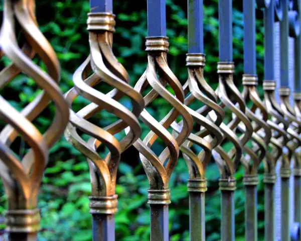 Detailaufnahme eines verzierten metallzauns, der darauf wartet, gestrichen zu werden. Die gedrehten Elemente glänzen im Licht.