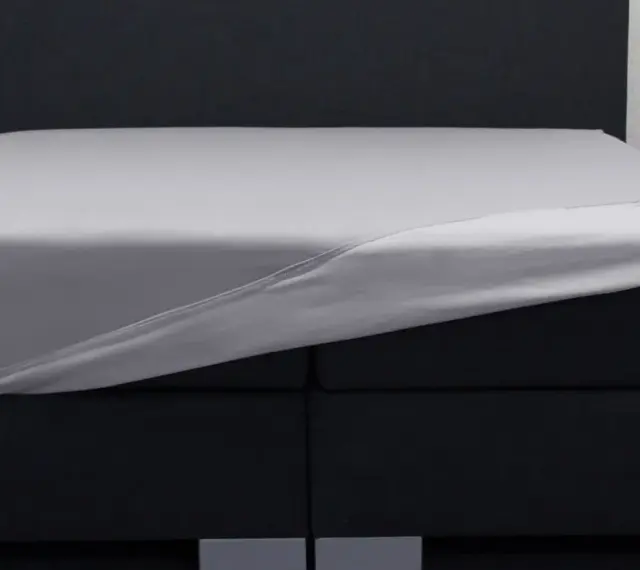 Ein graues Spannbettlaken wird über ein Boxspringbett gezogen. So beziehe ich ein Boxspringbett – einfach und schnell.