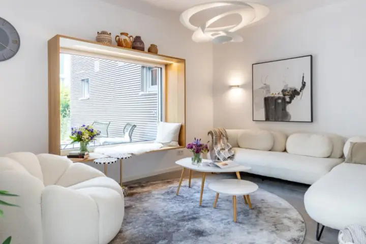 Modernes Wohnzimmer mit weißem Sofa, gemütlichem Sessel und einem Fensterplatz. Die schale dekorieren modern mit Vasen und Büchern.
