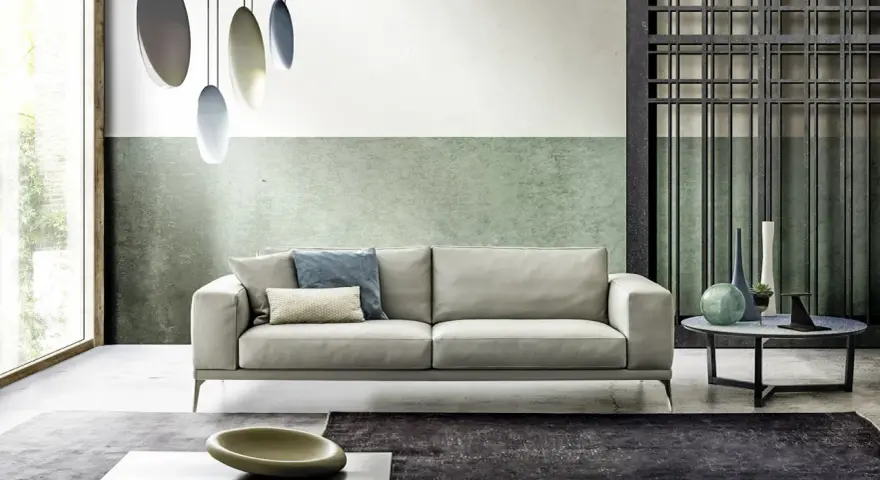 Modernes Wohnzimmer mit hellem Sofa, grüner Wand und stilvollem farbkonzept. Hängende Lampen und dekorative Vasen ergänzen das Ambiente.