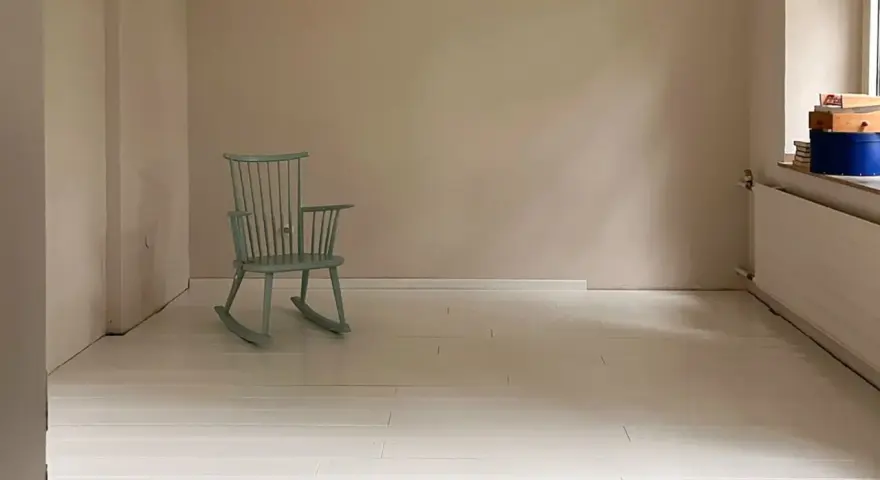Ein hell gestrichener holzboden mit einer mintgrünen Schaukelstuhl.