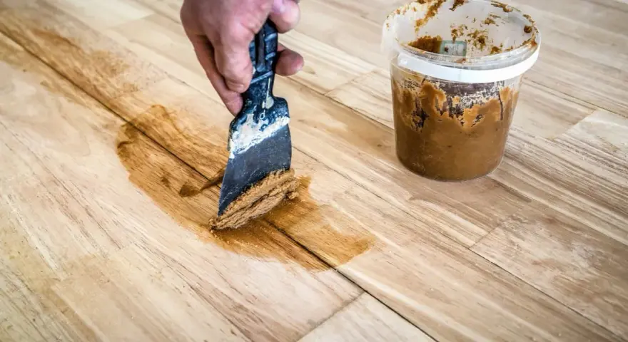Mit einem Spachtel und Holzpaste werden Kratzer aus einem Holztisch entfernt.