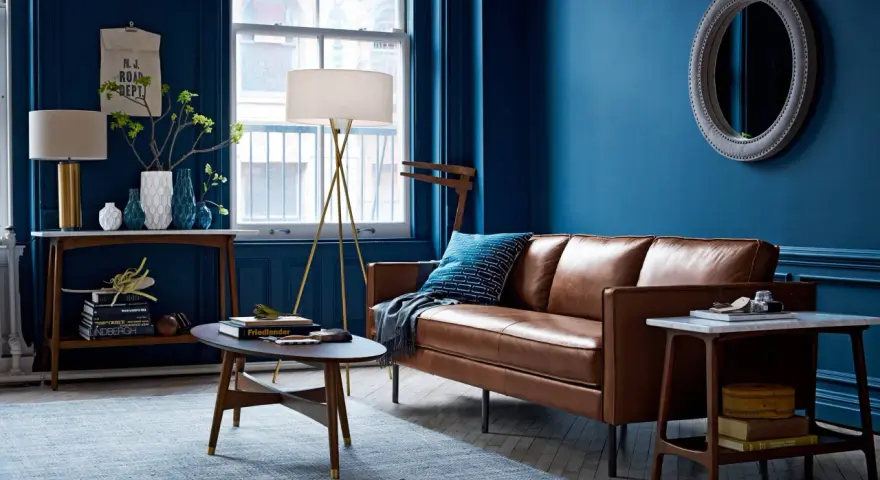 Gemütliches Wohnzimmer mit tiefblauen Wänden, brauner Ledercouch und einem hellblauen Teppich. Die Kombination aus Blau und Braun schafft eine warme Atmosphäre.