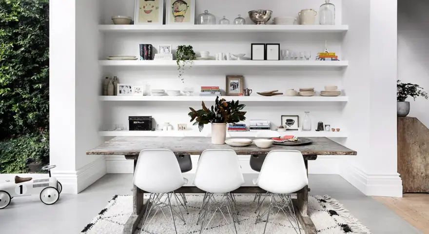 Moderne Esszimmer Wand Ideen: Weiße Regale voller Deko, Geschirr und Bilder über einem rustikalen Holztisch mit weißen Stühlen.
