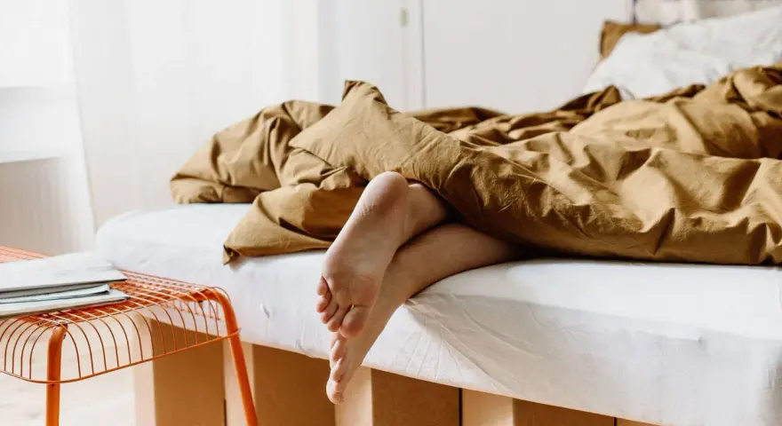 Füße ragen aus einem gemütlichen, braunen Bett hervor. Das Bett ist 210 cm lang und lädt zum Entspannen ein.