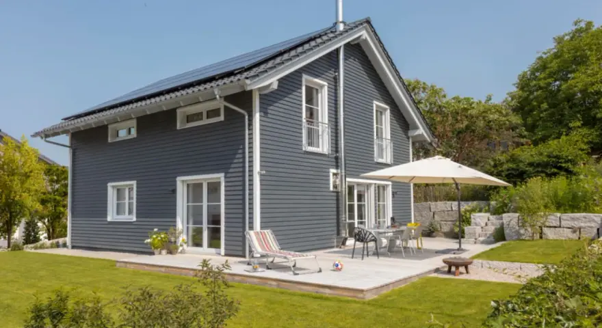 Modernes Haus mit dunkler Holzfassade, die zweifarbig gestrichen ist. Sonnige Terrasse mit Gartenmöbeln und Liegestuhl.