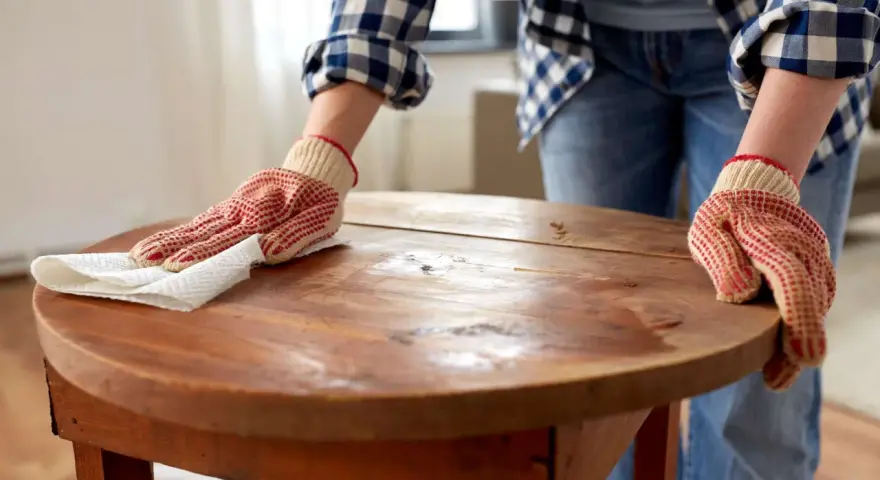 Person mit Handschuhen poliert einen alten Holztisch. Die Pflege des Holztisches ist wichtig, damit er lange schön bleibt.