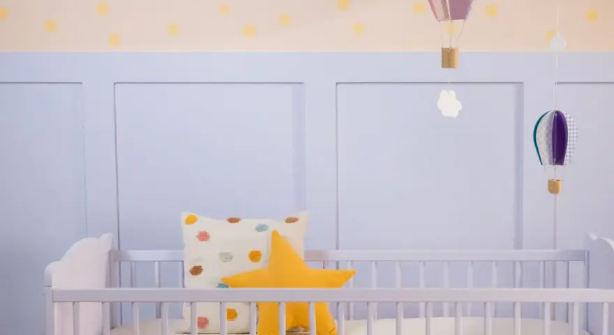 Ein frisch gestrichenes Kinderbett in zartem Lila, dekoriert mit bunten Kissen und schwebenden Heißluftballons.