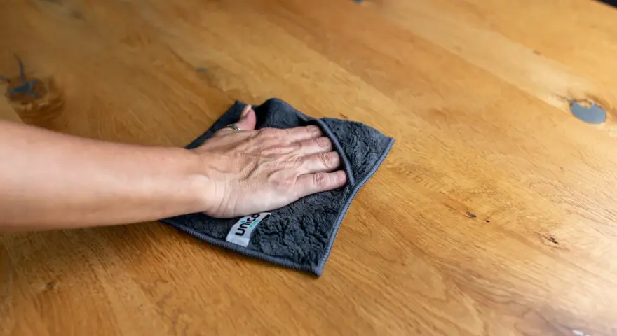 Hand wischt mit Tuch über Holzoberfläche, um schwarze Flecken zu entfernen. Hausmittel-Tipp für sauberes Holz.