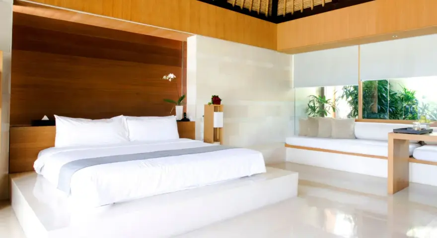 Luxuriöses Schlafzimmer mit einem großen weißen Bett, das den Unterschied zwischen einem King und Queen Bett verdeutlicht. Holzakzente und viel Licht.