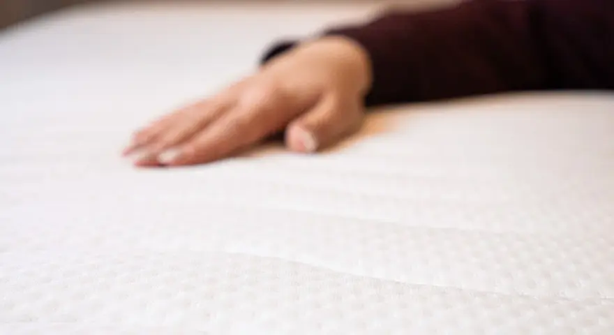 Eine Hand liegt auf einer weißen Matratze. Wann sollte man eine Matratze austauschen? Wenn sie durchgelegen ist oder Flecken hat.