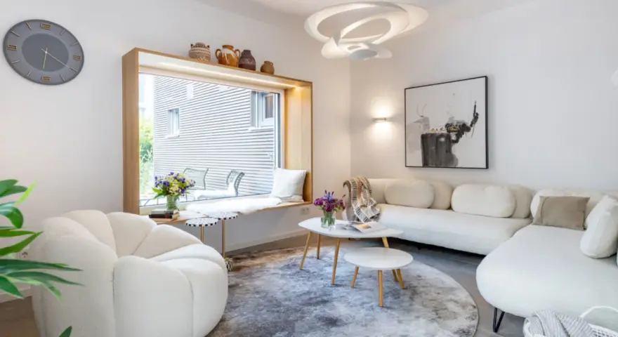 Modernes Wohnzimmer mit weißem Sofa, gemütlichem Sessel und einem Fensterplatz. Die schale dekorieren modern mit Vasen und Büchern.