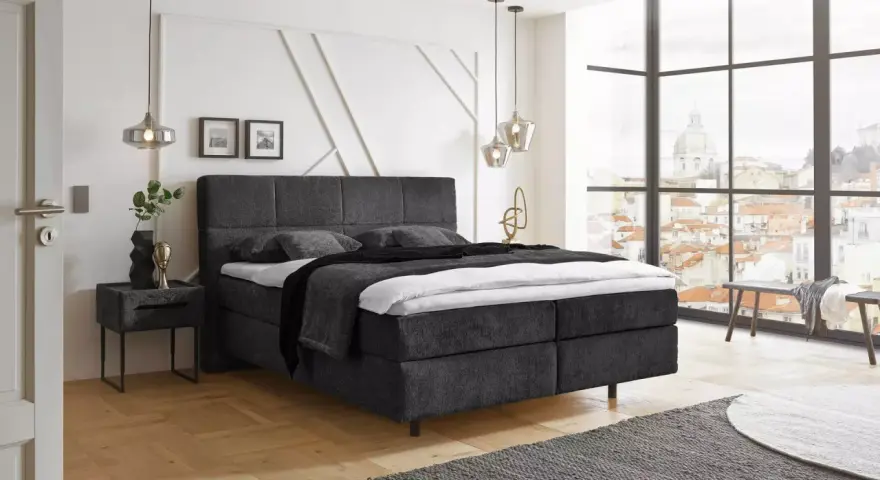 Ein modernes Schlafzimmer mit einem dunklen Boxspringbett ja oder nein? Helle Wände, Holzboden und ein Fenster mit Stadtblick.