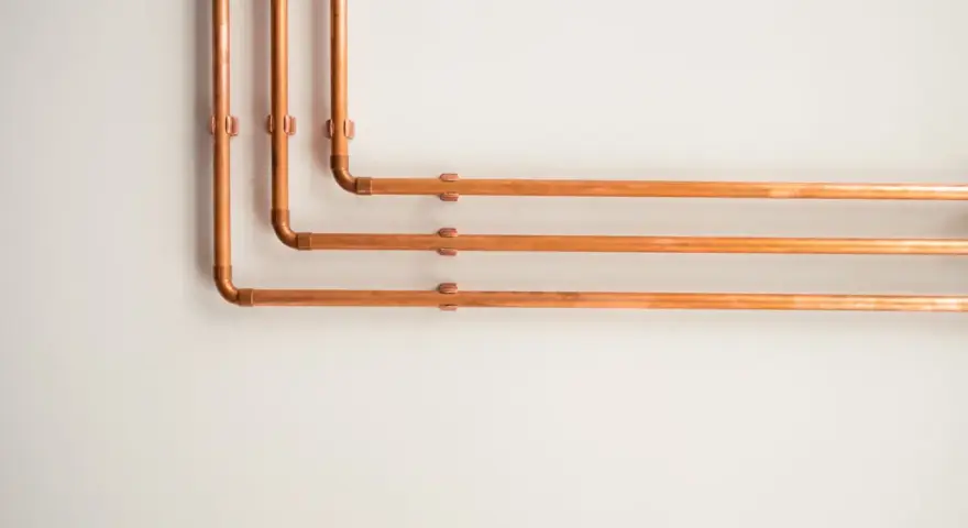 Kupferrohre an einer weißen Wand, die sich in einem rechten Winkel biegen. Tolle rohrverkleidung ideen für ein industrielles oder modernes Design.