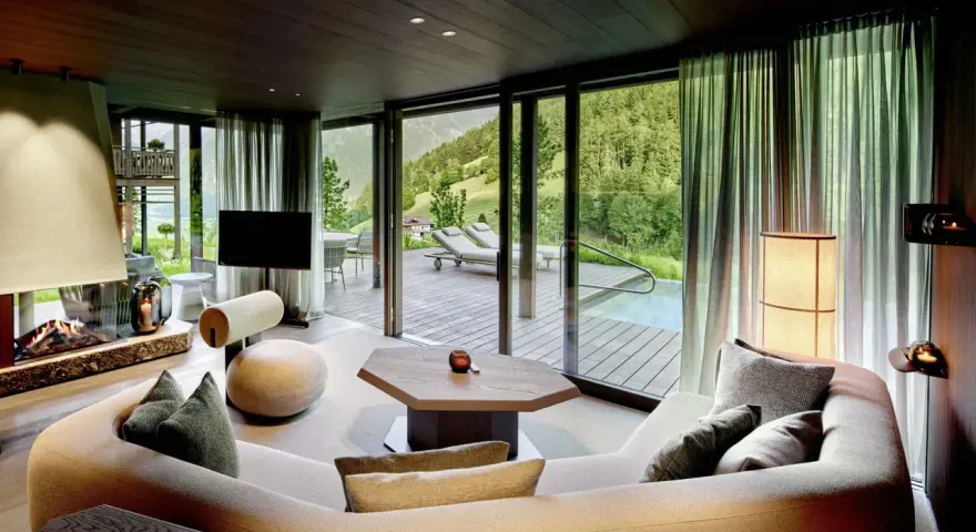 Gemütliches Wohnzimmer mit Kamin, großem Sofa und Bergblick. Die luxuriöse Chalet-Inneneinrichtung strahlt Wärme und Eleganz aus.
