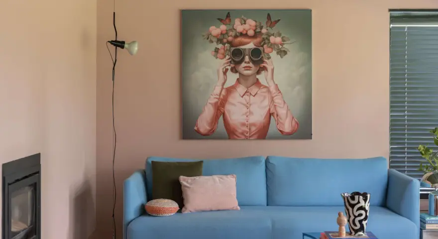 Ein blauer Sofa mit Kissen vor einer Wand mit einem surrealen Gemälde, das eine Frau mit Blumen und Schmetterlingen auf dem Kopf zeigt. Eine kreative Wandgestaltung, die zum Träumen einlädt.