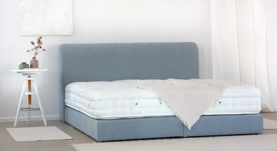 Ein Boxspringbett mit blauem Stoffbezug und weißer Matratze. So wird ein Boxspringbett geliefert: zerlegt und einfach aufzubauen.