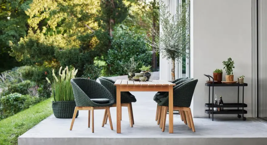 Einladende Sitzgruppe auf einer modernen Terrasse, perfekt für die nächste terrasse renovieren. Grüne Korbsessel und Holztisch laden zum Verweilen ein.