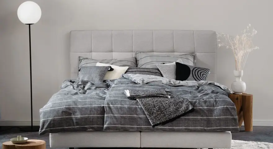 Stilvolle Schlafzimmer Ideen mit einem grauen Boxspringbett, gestreifter Bettwäsche und modernen Akzenten.
