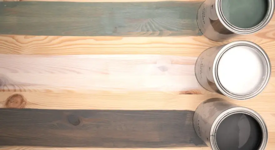 Holzlasur vorher nachher: drei Holzbretter mit unterschiedlichen Lasuren – grün, weiß und grau – und die passenden Dosen.