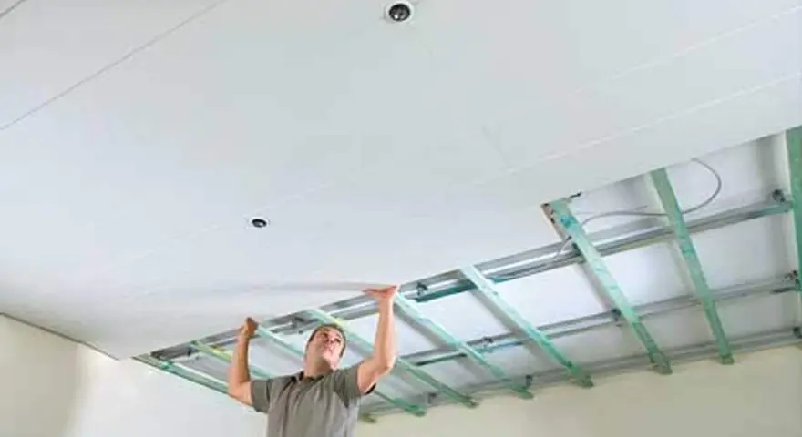 Mann verkleidet die Decke mit Gipskartonplatten. Die Unterkonstruktion ist sichtbar.