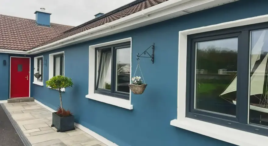 Ein blaues Haus mit roten Tür und dunklen Kunststofffenstern. Die Fensterrahmen sind in einem eleganten Anthrazit gehalten, was die modernen Kunststofffenster Farben unterstreicht.