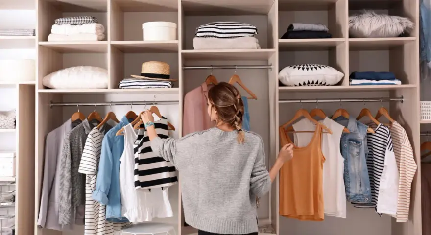 Frau sortiert Kleidung in einem offenen Schrank. Sie überlegt, was sie anziehen soll, um den offenen Schrank zu verkleiden.