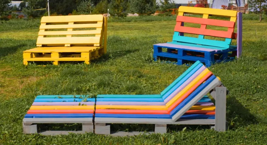 Bunte Palettenmöbel im Garten: Eine gelbe Bank, eine mehrfarbige Sitzbank und eine bunte Liege laden zum Entspannen ein. Paletten streichen ohne schleifen ist hier die Devise.