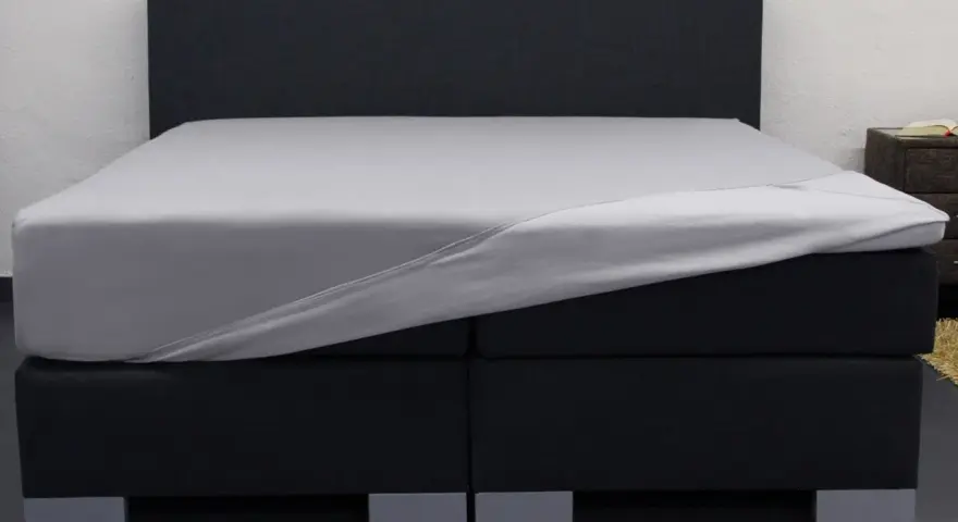 Ein graues Spannbettlaken wird über ein Boxspringbett gezogen. So beziehe ich ein Boxspringbett – einfach und schnell.