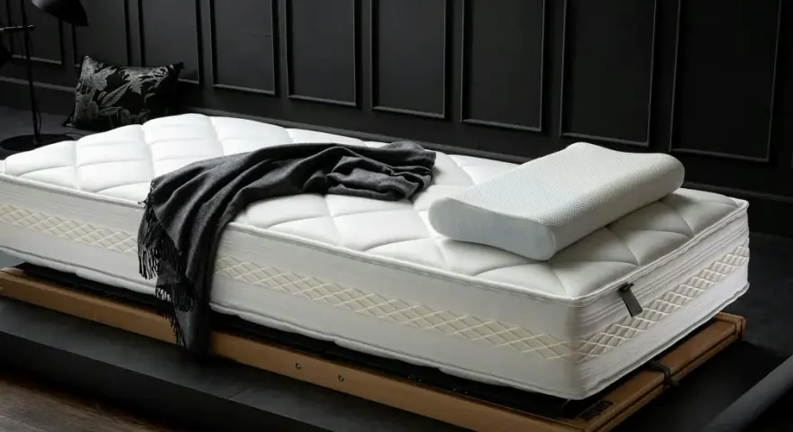 Eine neue, weiße Matratze mit Kissen und Decke liegt auf einem Holzrahmen. Zeit für einen Matratzenwechsel für erholsamen Schlaf.