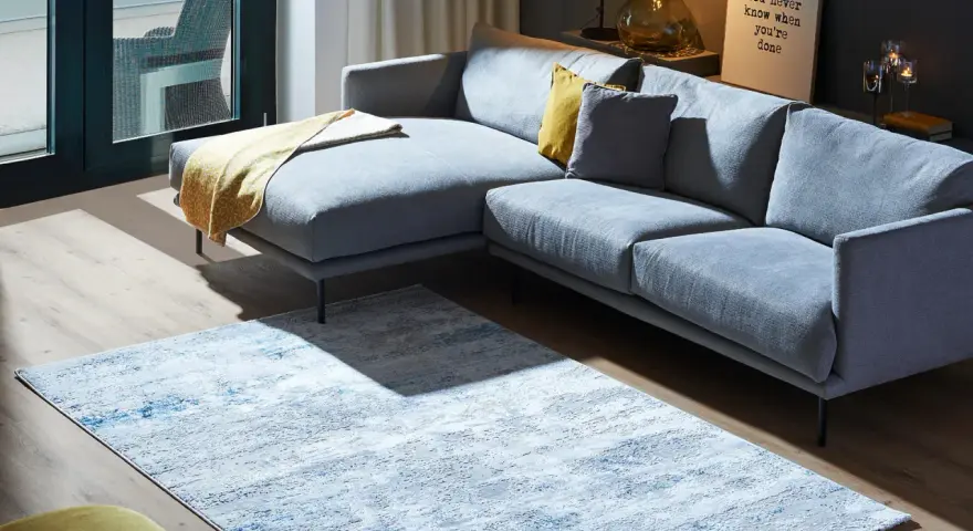 Ein moderner Wohnbereich mit einem grauen Ecksofa und einem Teppich, der richtig platziert unter dem Sofa liegt.
