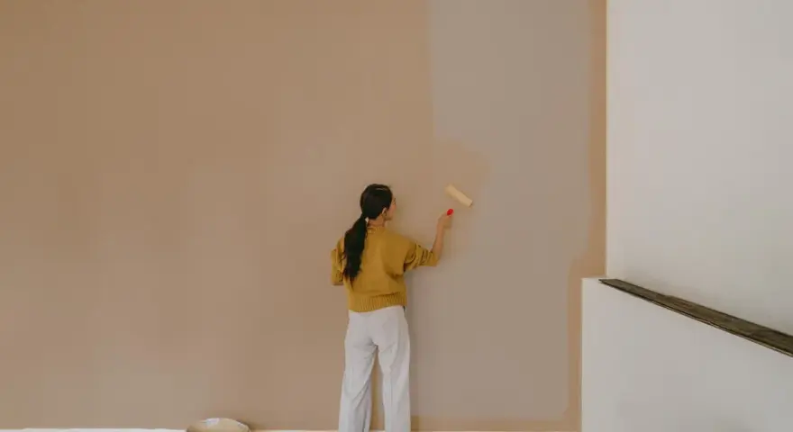 Frau streicht Wand mit neuer Farbe. Man fragt sich, wie lange braucht wandfarbe zum trocknen, während die alte Farbe noch sichtbar ist.