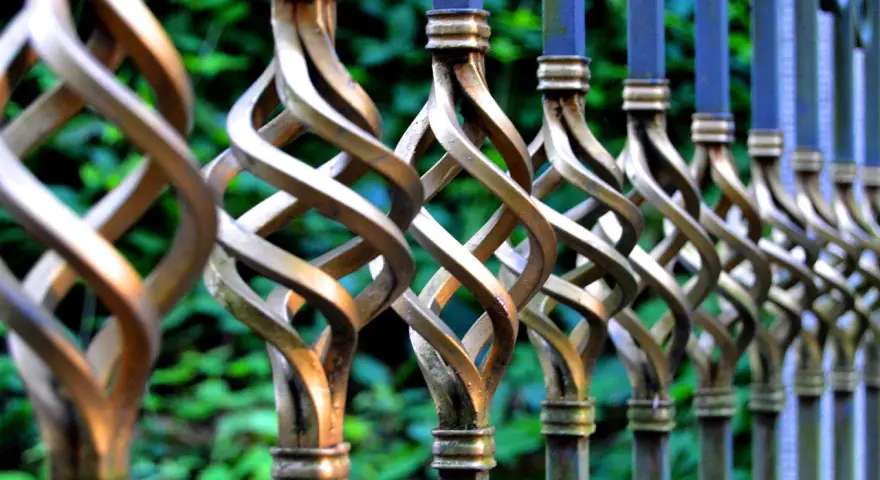 Detailaufnahme eines verzierten metallzauns, der darauf wartet, gestrichen zu werden. Die gedrehten Elemente glänzen im Licht.