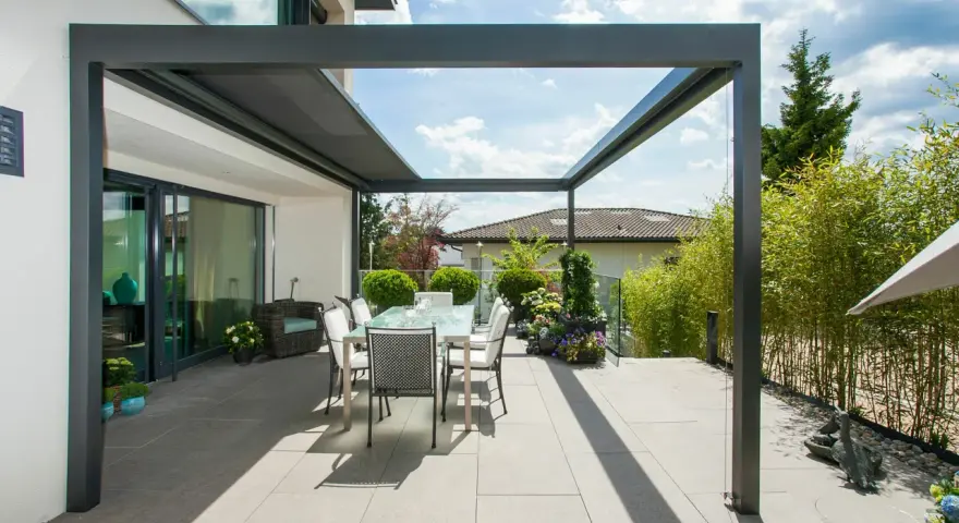 Moderne Terrassenbeschattung Ideen: Ein Essbereich unter einer Pergola mit Glasdach, umgeben von Bambus und Blumen.